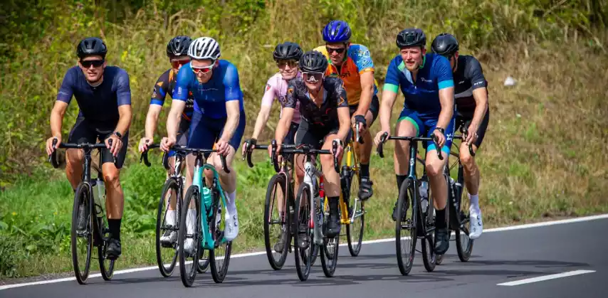 Zes wielrenners fietsen samen over een rustige weg door het groene landschap.