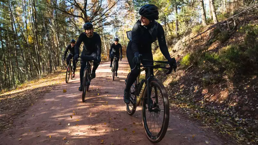 Gravelbikers fietsen over een breed onverhard bospad tussen de bomen.